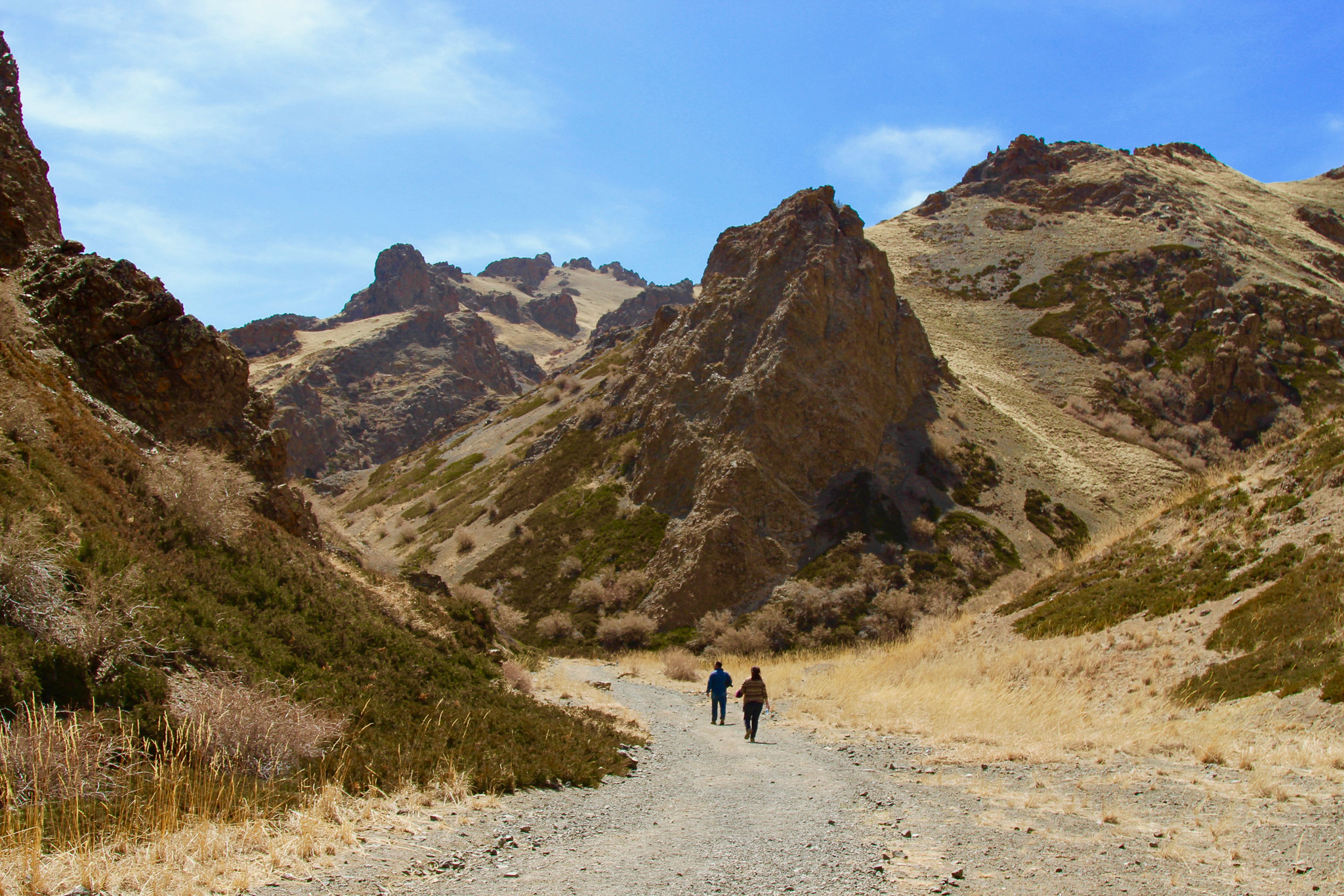Hikers walk a dirt path between rocky mountains in Mongolia