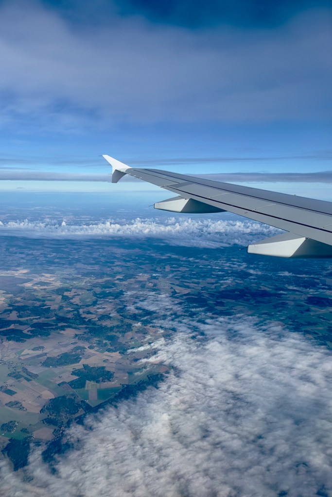 Airplane wing over clouds and patchwork farmland seen from a window seat